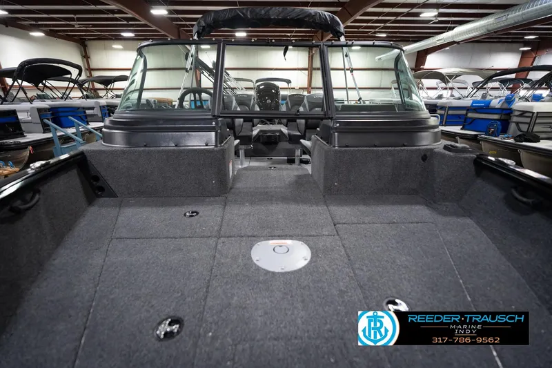 Slide: The Image of 2026 Lund 1875 Impact XS boat interior in showroom, featuring spacious deck and windshield. - 19