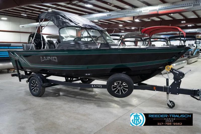 Slide: The Image of 2026 Lund 1875 Impact XS boat on trailer in showroom, black and green design. - 6