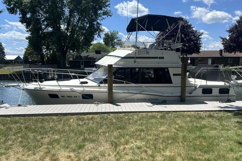 The Image of 1985 Carver 3207 Aft Cabin yacht docked by a grassy shore under a blue sky. - 1