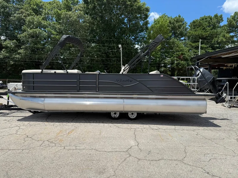 The Image of 2026 Bentley Pontoons Legacy 243 Swingback on trailer, parked outdoors, surrounded by trees. - 0