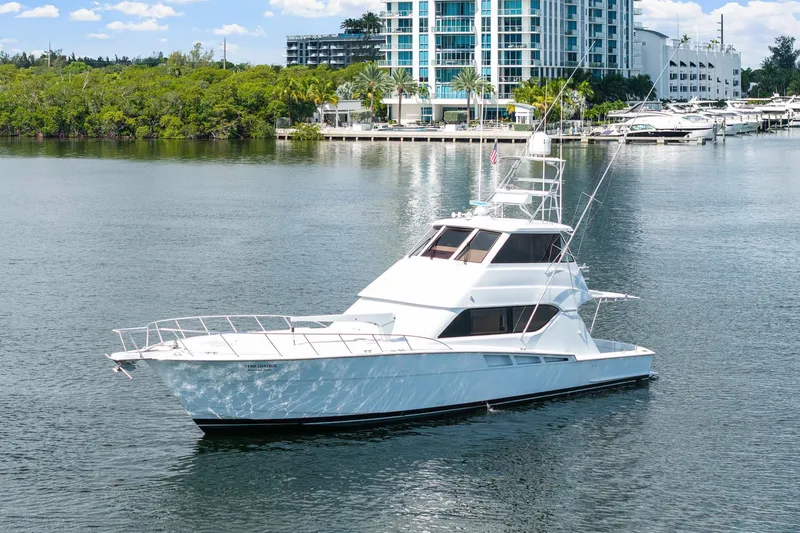 Slide: The Image of 2002 Hatteras 60 Convertible yacht on calm water near a marina and modern buildings. - 10