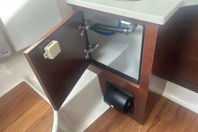 Slide: The Image of 2026 Chaparral 280 OSX boat interior cabinet with open door and visible plumbing. - 38