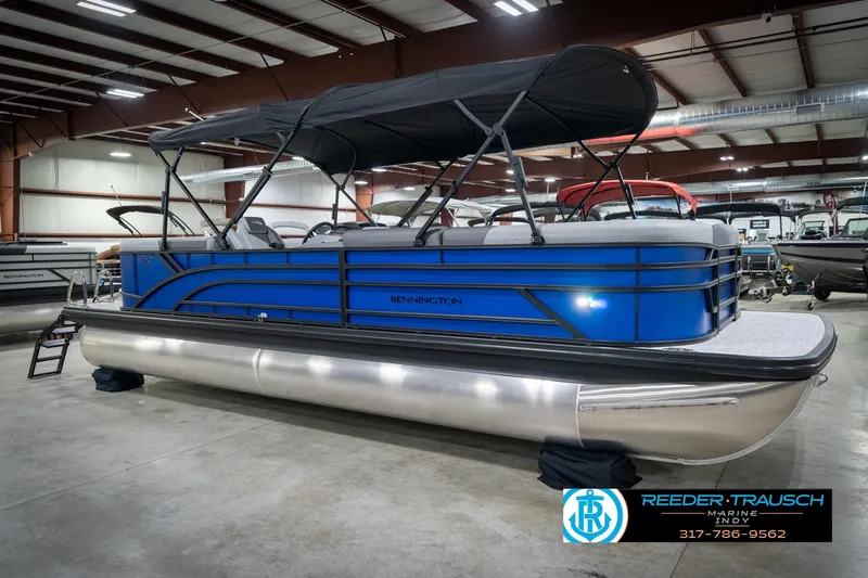 Slide: The Image of 2026 Bennington 25 SSR pontoon boat in showroom with blue exterior and black canopy. - 6