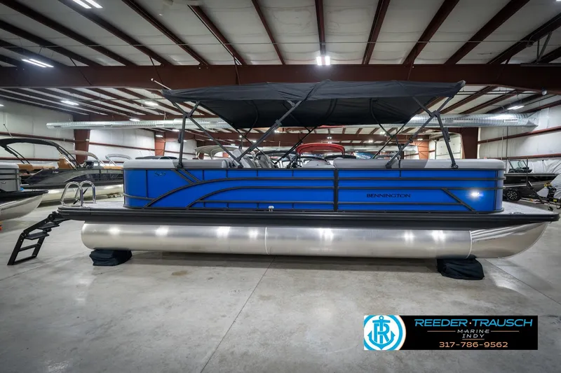Slide: The Image of 2026 Bennington 25 SSR pontoon boat in showroom, featuring sleek blue design and canopy. - 7