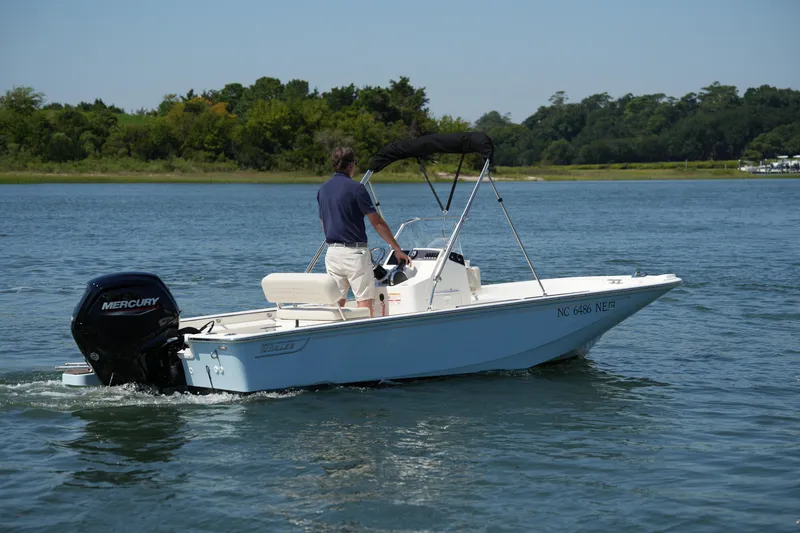 Slide: The Image of 2025 Boston Whaler 170 Montauk boat cruising on a serene lake with lush greenery. - 2