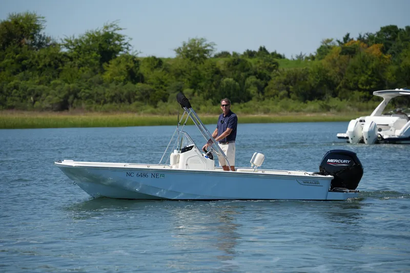 Slide: The Image of 2025 Boston Whaler 170 Montauk boat on water, man steering, lush greenery background. - 4