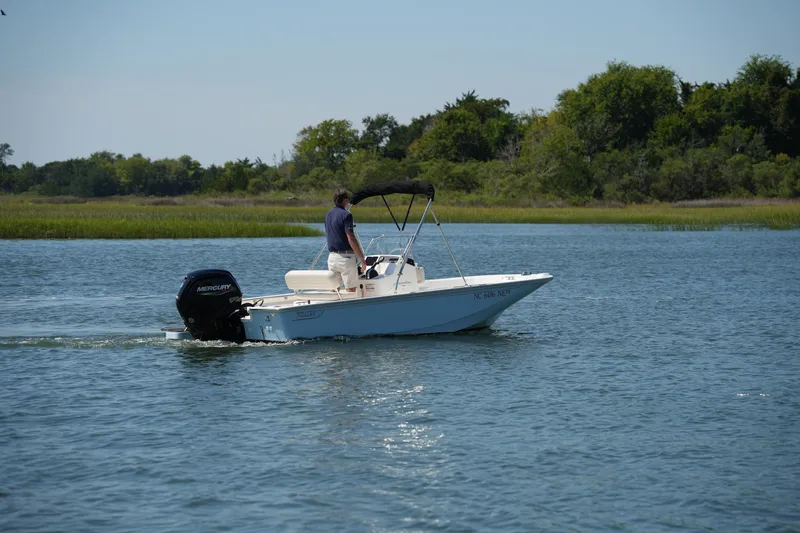 Slide: The Image of 2025 Boston Whaler 170 Montauk boat cruising on a serene lake with lush greenery. - 6