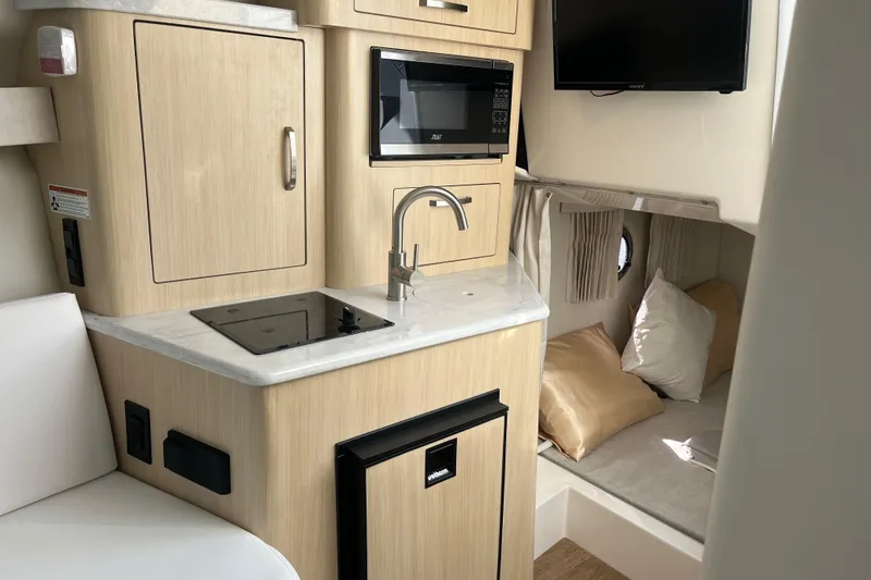 Slide: The Image of 2023 Regal 28 Express boat interior with kitchenette, microwave, and cozy sleeping area. - 27