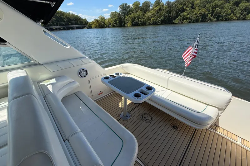 Slide: The Image of 1995 Sea Ray 330 Sundancer boat interior with seating, table, and American flag on a lake. - 10