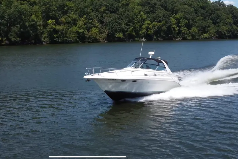 Slide: The Image of 1995 Sea Ray 330 Sundancer cruising on a scenic lake with lush green forest backdrop. - 2