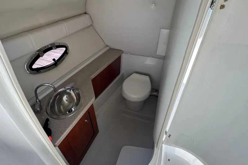 Slide: The Image of 2012 Crownline 305 SS boat bathroom with sink, toilet, and porthole window. - 12