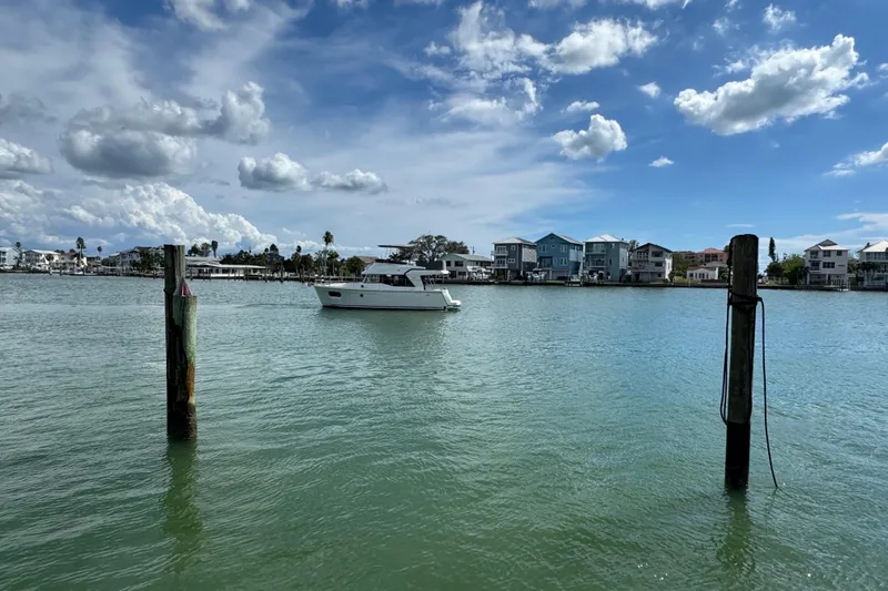 Slide: The Image of 2023 Beneteau Swift Trawler 35 on calm water, with coastal homes and cloudy sky. - 2