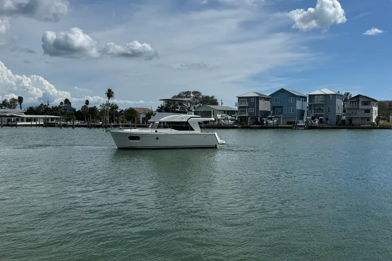 Slide: The Image of 2023 Beneteau Swift Trawler 35 cruising on a calm waterway near waterfront homes. - 3