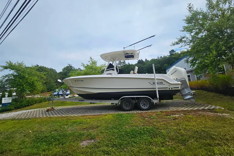 Slide: The Image of 2019 Boston Whaler 230 Outrage boat on trailer, parked outdoors with trees in background. - 0
