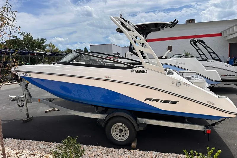 Slide: The Image of 2024 Yamaha Boats AR195 on trailer, blue and white design, parked outdoors. - 0