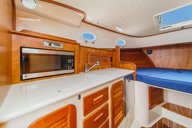 Slide: The Image of 2014 Hinckley Talaria 34 interior with wood cabinetry, microwave, sink, and blue cushioned seating. - 25