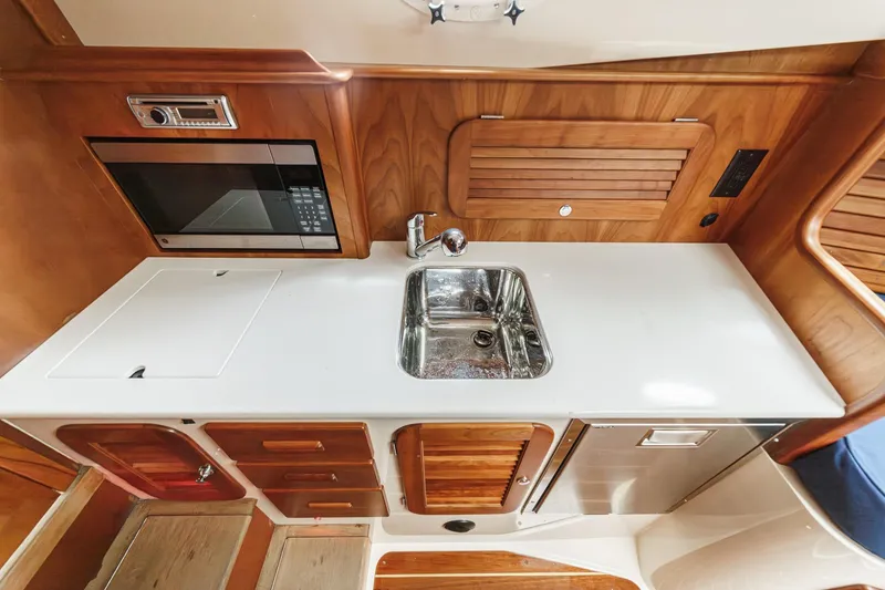 Slide: The Image of 2014 Hinckley Talaria 34 yacht interior kitchen with sink, microwave, and wooden cabinetry. - 27