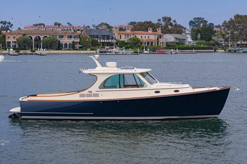 Slide: The Image of 2014 Hinckley Talaria 34 yacht on calm water, elegant design, luxury waterfront homes in background. - 6