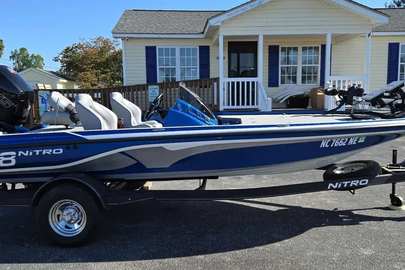 Slide: The Image of 2024 Nitro Z18 boat in blue, parked on a trailer in front of a house. - 2