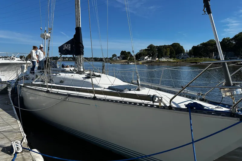 Slide: The Image of 1988 C&C 44 sailboat docked by a serene waterfront, clear blue sky. - 28