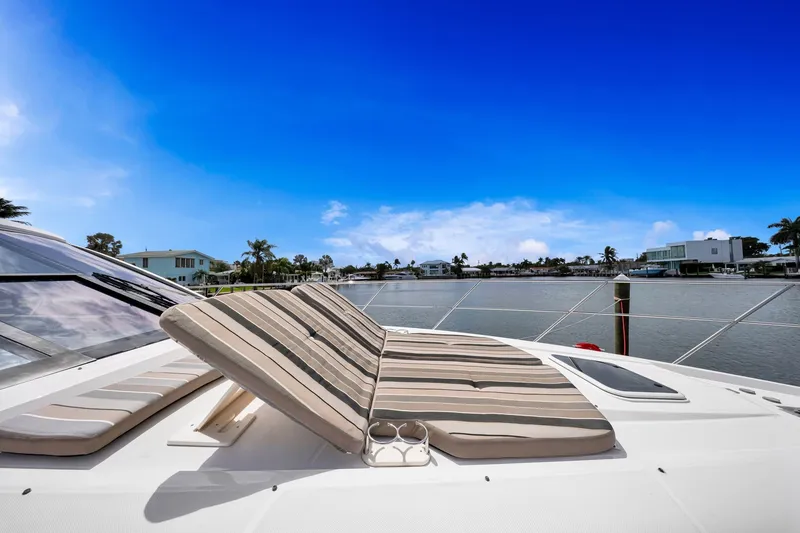 Slide: The Image of 2017 Regal 53 Sport Coupe yacht with striped sun loungers on deck, overlooking serene waterfront. - 10