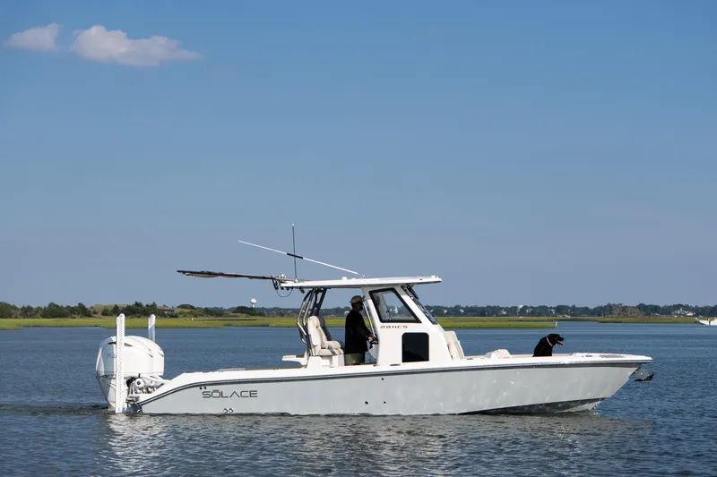 Slide: The Image of 2026 Solace 28 HCS boat on calm water with a person and a dog onboard. - 0