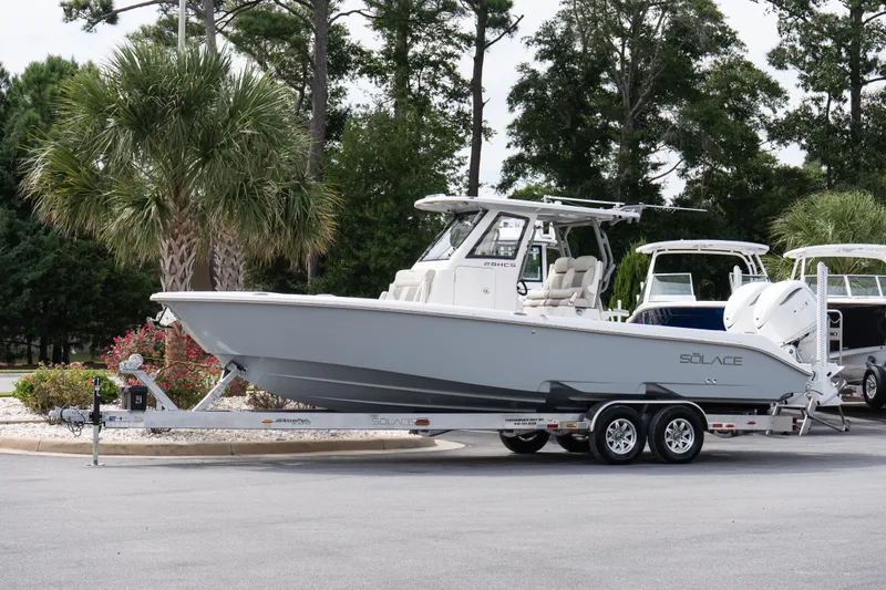 Slide: The Image of 2026 Solace 28 HCS boat on trailer, parked outdoors with trees in background. - 12