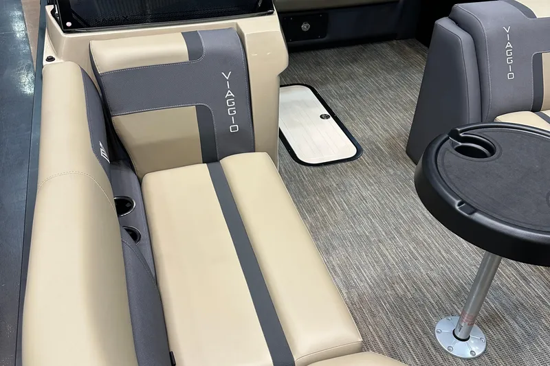 Slide: The Image of 2026 Viaggio Lago X22D Tritoon interior with beige and gray seating, cup holders, and table. - 14