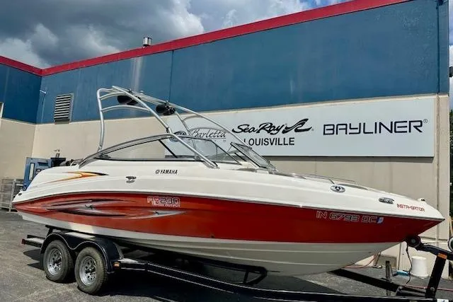 The Image of 2007 Yamaha AR 230 boat on trailer, parked outside dealership with blue and red building. - 1