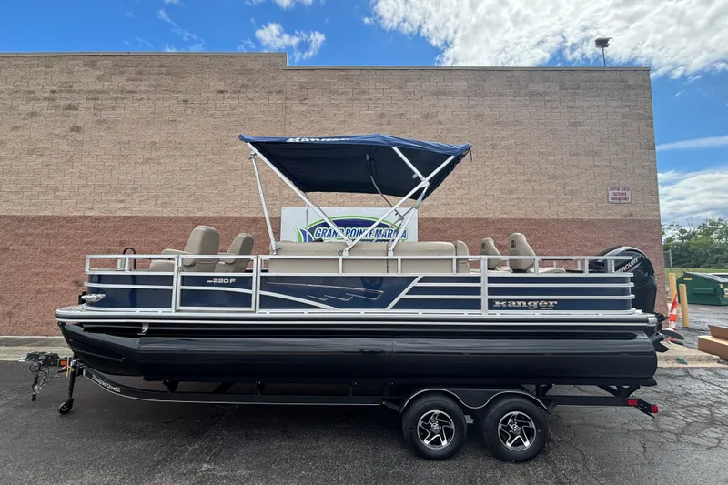 Slide: The Image of 2025 Ranger 220F pontoon boat with canopy on trailer, parked outdoors. - 0