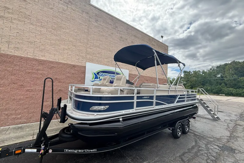 Slide: The Image of 2025 Ranger 220F pontoon boat on trailer, parked outdoors under cloudy sky. - 1