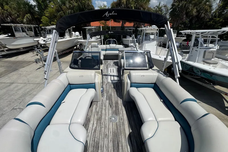 Slide: The Image of 2019 Avalon Catalina Platinum Elite pontoon boat with spacious seating and windshield, docked among other boats. - 14