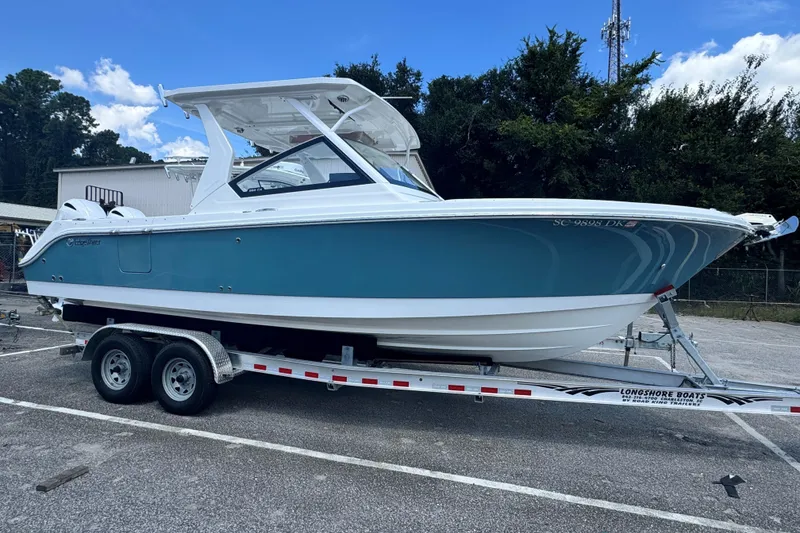 Slide: The Image of 2019 Edgewater 262 CX boat on trailer, blue and white design, parked outdoors. - 0