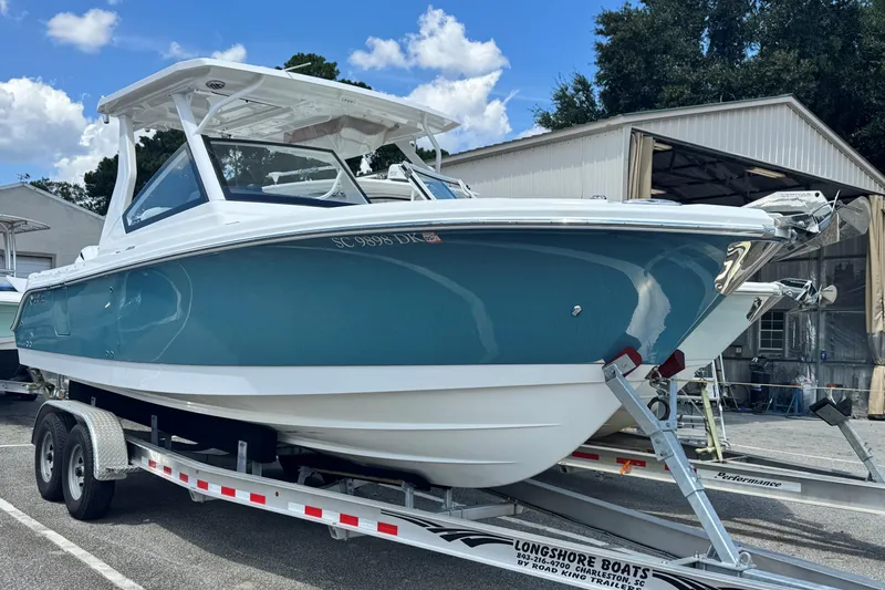 Slide: The Image of 2019 Edgewater 262 CX boat on trailer, blue and white, parked near a warehouse. - 1