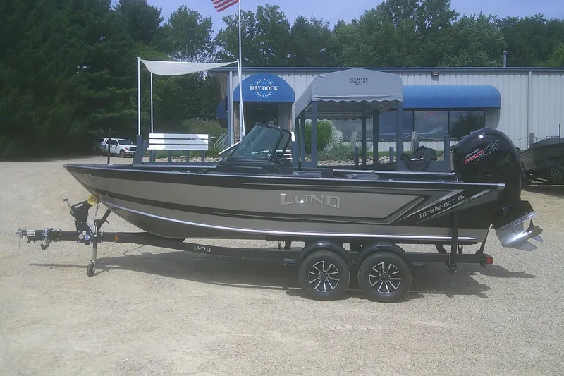 Slide: The Image of 2026 Lund 1875 Impact XS Sport boat on trailer, parked outside dealership. - 1