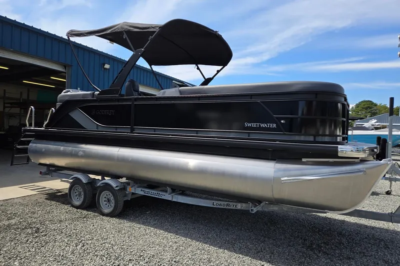 Slide: The Image of 2026 Godfrey SWEETWATER 2286 SB pontoon boat on trailer, parked outside a blue building. - 1