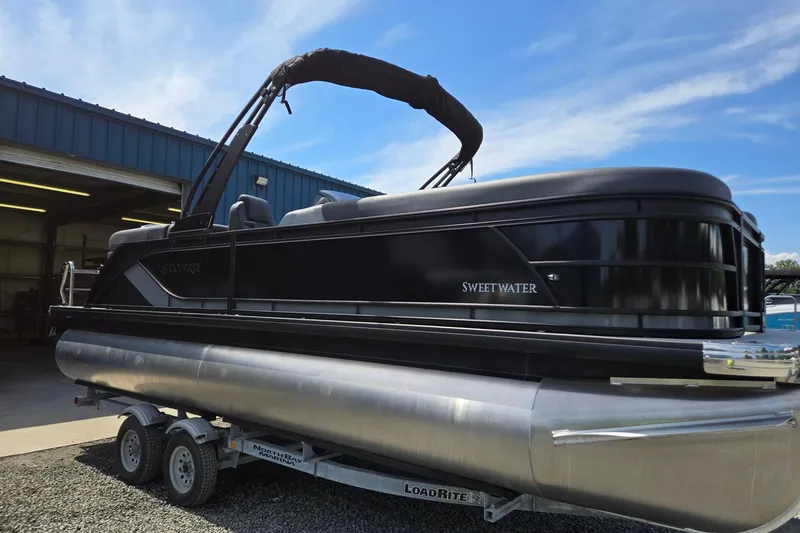 Slide: The Image of 2026 Godfrey SWEETWATER 2286 SB pontoon boat on trailer, parked outside a blue building. - 10