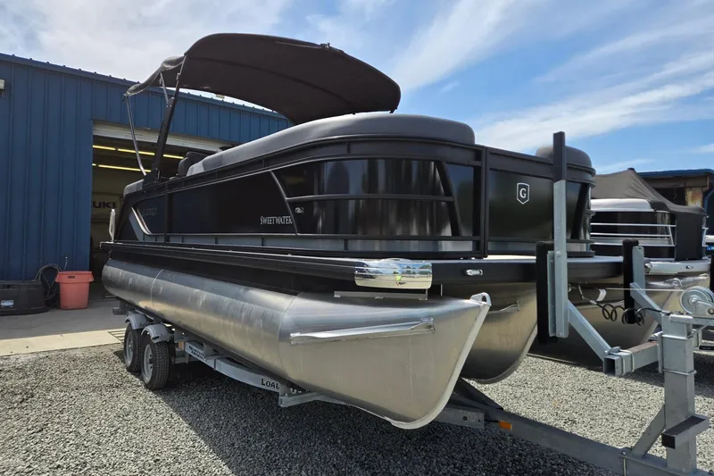 Slide: The Image of 2026 Godfrey SWEETWATER 2286 SB pontoon boat on trailer, parked outside blue building. - 2