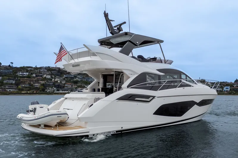 Slide: The Image of 2021 Sunseeker Manhattan 55 yacht cruising near coastal homes, featuring sleek design and American flag. - 11
