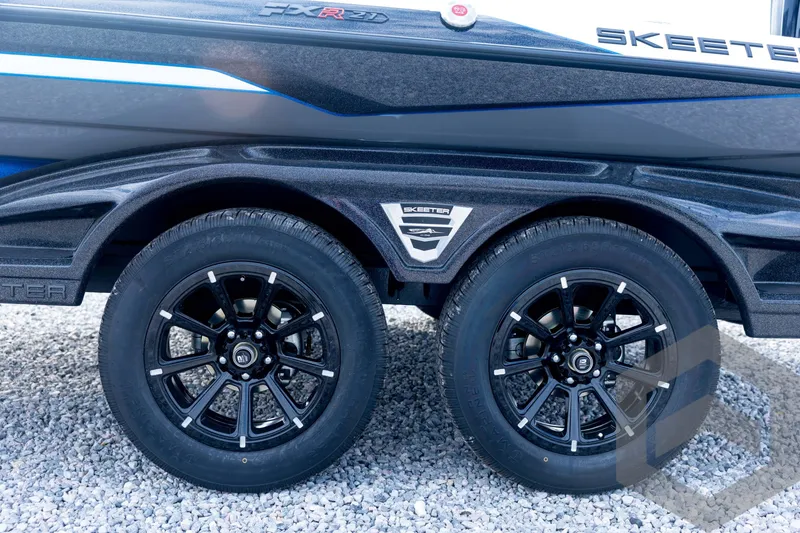 Slide: The Image of 2026 Skeeter FXR21 FLEX boat trailer with dual black alloy wheels on gravel. - 32