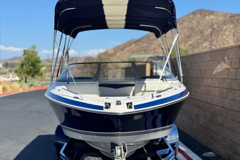 Slide: The Image of 2010 Four Winns H210 boat with canopy, parked on a sunny day near mountains. - 2