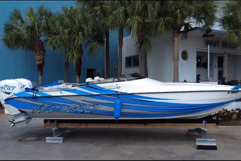 Slide: The Image of 2021 Velocity 290sc speedboat with blue stripes, docked near palm trees. - 6