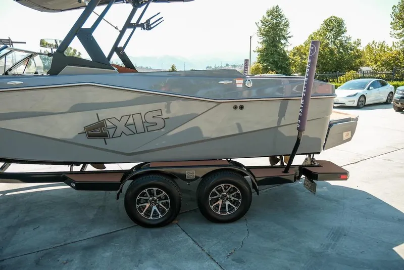 Slide: The Image of 2024 Axis T220 boat on trailer, parked outdoors with trees and cars in the background. - 11