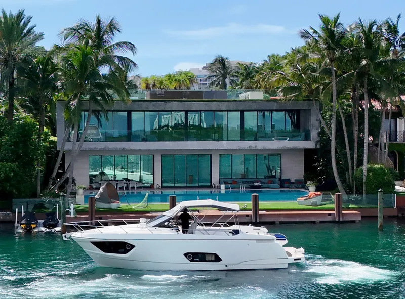 The Image of Luxury yacht Absolute 40 cruising near modern waterfront mansion, surrounded by palm trees. - 0
