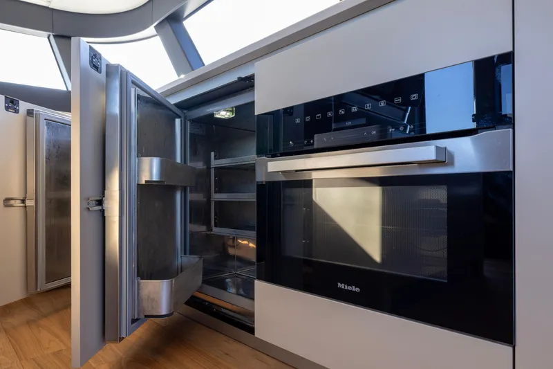 Slide: The Image of Modern kitchen appliances on 2024 Bluegame BGX63 yacht, featuring Miele oven and open refrigerator. - 79