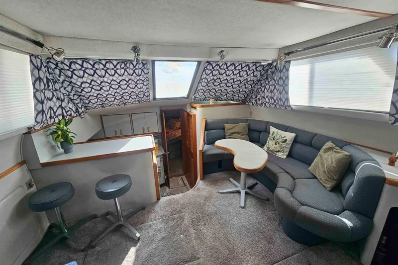 Slide: The Image of 1990 Sea Ray 440 Aft Cabin interior with cozy seating, patterned curtains, and a small table. - 17