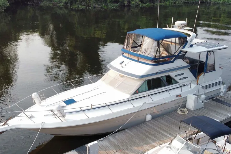 Slide: The Image of 1990 Sea Ray 440 Aft Cabin yacht docked on calm water, featuring a blue canopy. - 2