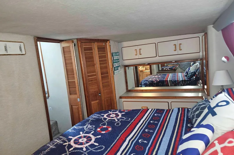 Slide: The Image of 1990 Sea Ray 440 Aft Cabin bedroom with nautical-themed bedding and wooden cabinetry. - 23