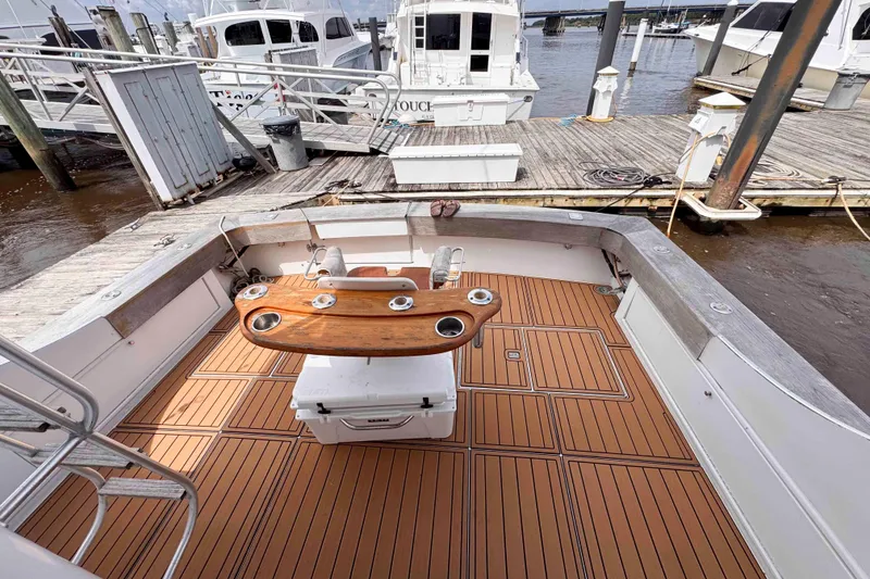 Slide: The Image of 1989 Buddy Davis 47 boat deck with wooden flooring and fishing rod holders at a marina. - 18