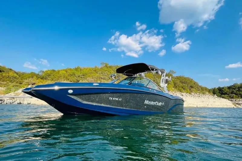 Slide: The Image of 2019 MasterCraft X26 boat on a sunny lake with clear blue skies. - 3